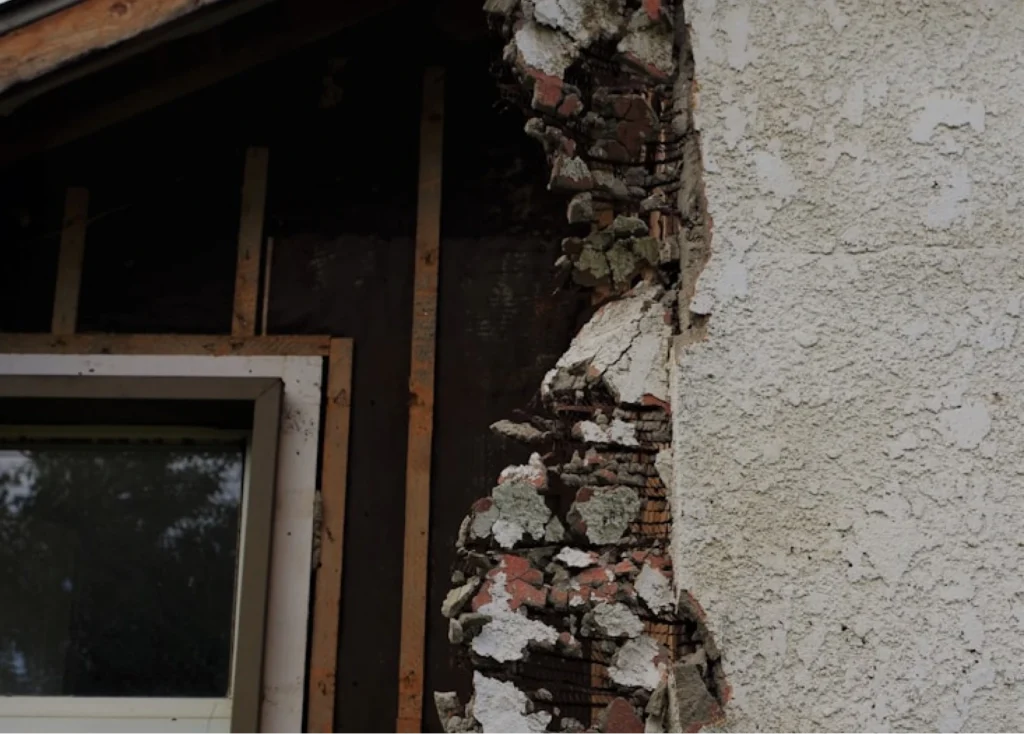 Damaged external wall with render broken away exposing brickwork